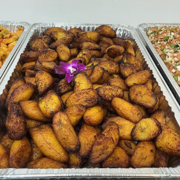 A catering tray filled with golden-brown fried plantains, garnished with a purple orchid.