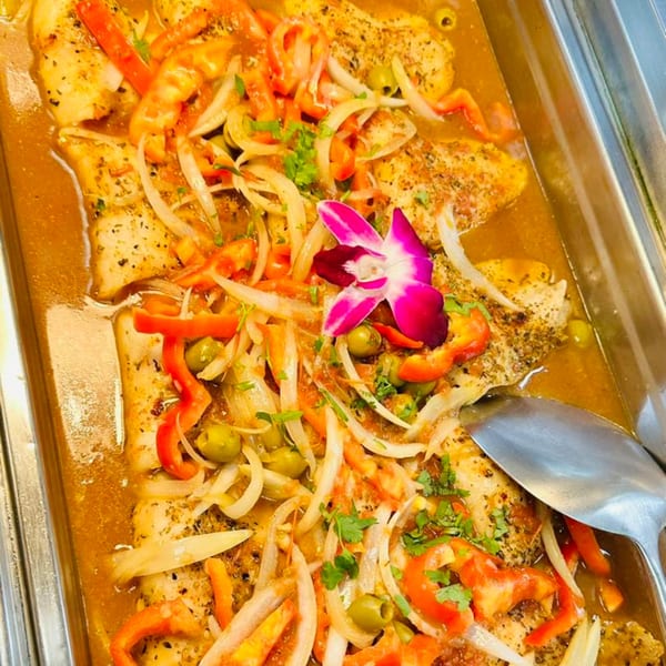 Latin-American fish dish with peppers, onions, olives, and a pink orchid garnish in a serving tray.