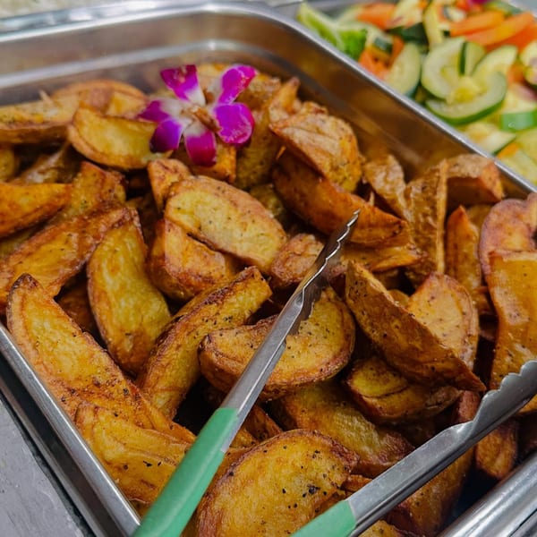 Golden-brown potato wedges with seasoning and a purple orchid garnish in a serving tray.