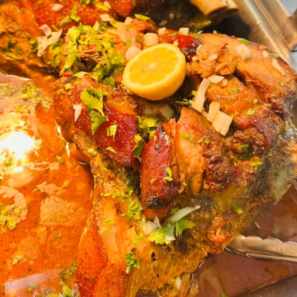 Close-up of roasted Latin American meat dish with a lemon slice, cilantro, and onions.