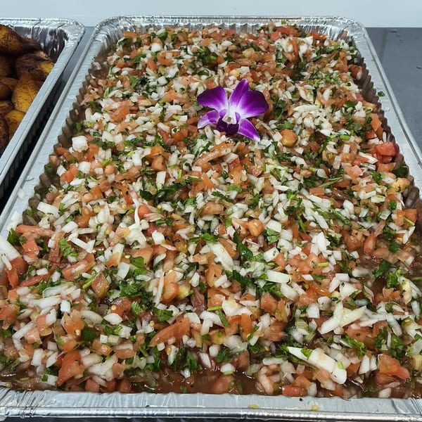 A large tray of fresh pico de gallo with a purple orchid garnish, next to a tray of plantains.