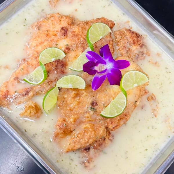 Crispy fried fish fillets in a creamy sauce, garnished with lime slices and a purple orchid.