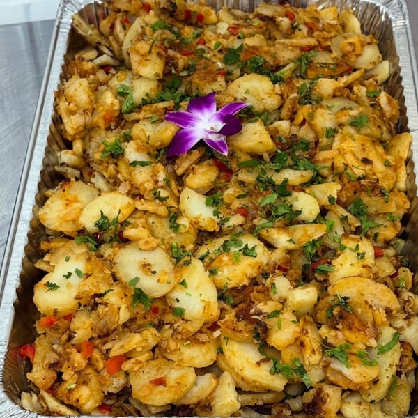 A catering tray of crispy fried potatoes with red peppers, cilantro, and a purple orchid garnish.