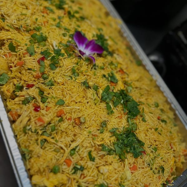 A large tray of yellow rice with peas, carrots, and cilantro, garnished with a purple orchid.